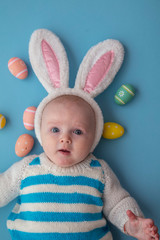 Cute baby wearing easter bunny ears surrounded by easter eggs.