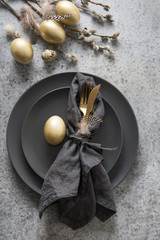 Easter table setting with black and golden decor on grey. Top view.