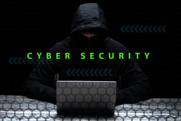 hacker in hood using laptop near cyber security lettering on black