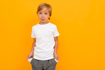 Cute little boy in t-shirt and trousers holds his hands in pockets isolated on yellow background