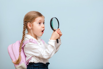 Cheerful young blonde baby girl looks through a magnifying glass. isolated on a blue background....
