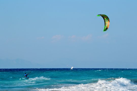 Ixia, Rhodes, Greece. A kiteboarder harnesses the power of the wind with a large controllable power kite to be propelled across the sea water. Pebble beach in Paralia/Ixia