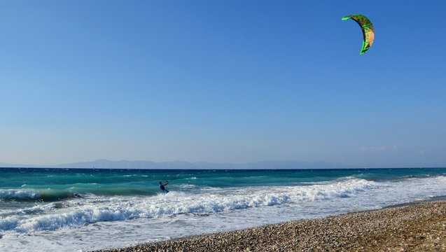 Ixia, Rhodes, Greece. A kiteboarder harnesses the power of the wind with a large controllable power kite to be propelled across the sea water. Pebble beach in Paralia/Ixia