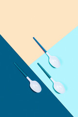 Dangerous three plastic spoons. Tricolor background. Flat lay, top view, copy space.