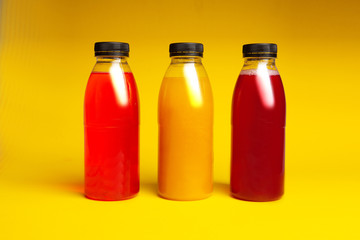 three plastic bottles with a drink of different colors on a yellow background
