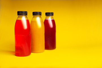 three plastic bottles with a drink of different colors on a yellow background