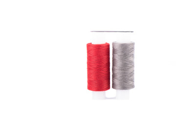 Close-up photo of a spool with red and gray thread and a needle isolated over white background.