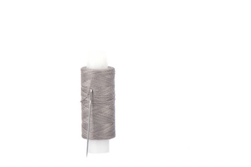 Close-up photo of a spool with gray thread and a needle isolated over white background.