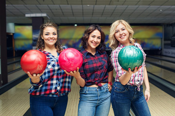 Three fun attractive girlfriends hold bowling balls and look at you