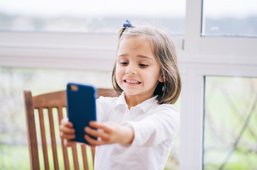A little girl takes a picture with the mobile phone smartphone at home