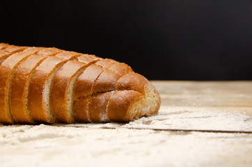Sliced loaf close up on a wooden table with flour on a black background with copy space