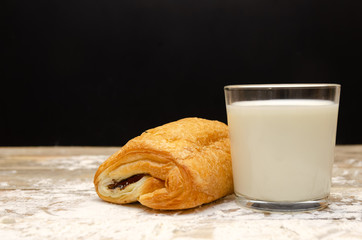 glass of milk and a bun on a wooden background with flour on a black background close up with a copy of the space