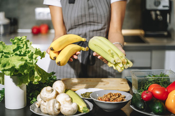 Close up of female hands holding fresh celery and bananas in the kitchen. Proper nutrition and health concept.