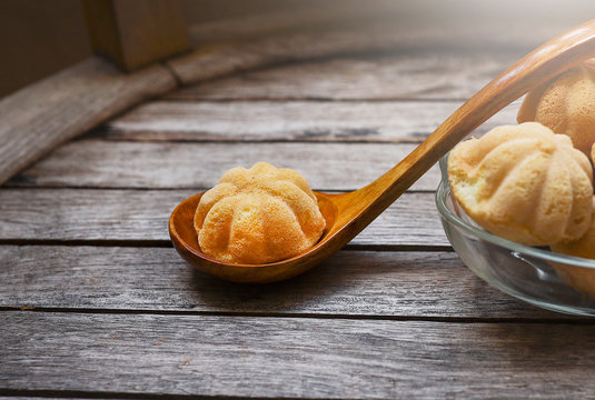 A bowl of kuih Bahulu or Baulu with spoon on wooden table.  Kuih Bahulu or Baulu is the Malaysian sponge cake made from eggs, sugar and flour among others.