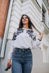 a young girl with brown hair in a white blouse and blue jeans walks down the street