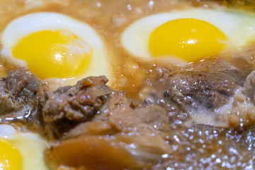 Fried eggs and pieces of meat in a frying pan in sunflower oil close-up. concept of homemade food