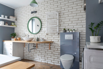 Interior of bathroom in loft apartment in white and grey color. Brick wall, grey decor, round...