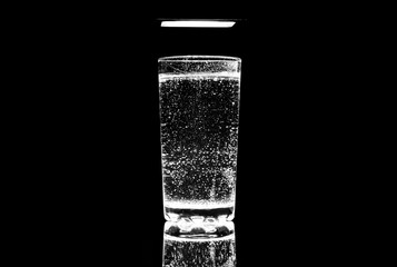 A glass of water on a black background and a bright light close-up. 