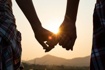 Close up of loving couple holding hands while walking at sunrise sunset in the meadow mountain in...