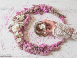 Flowers composition. girl's hand holds a glass of tea in a composition of pink flowers on a white background. Top view, flat lay.