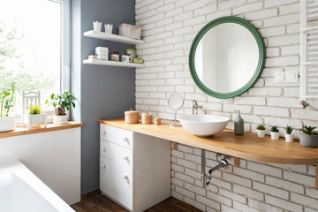 Bright interior of bathroom with window and white brick wall. Stylish interior with round mirror...