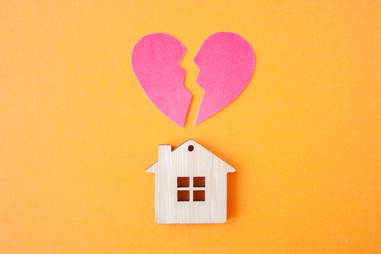 Divorce, division of property, poverty and no money concept. Wooden house with broken heart on bright orange  background. Mortgage, rent, realtor