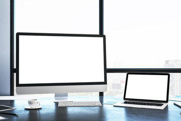 Computer and laptop with blank screen in modern office interior