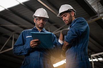 Factory technicians are discussing or planning work. They wear uniforms, safety helmets, and protective goggles. And look at the clipboard with details of the work.