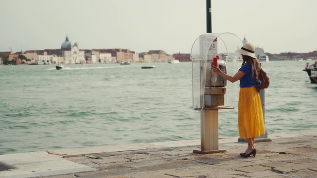 VENICE, ITALY - MAY 21, 2019: Lady in hat comes to old telephone booth to call