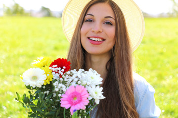 Gorgeous young woman holds bouquet of flowers and looks at camera in a field on spring