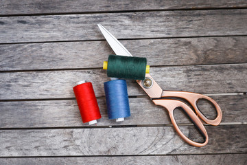 Threads and a pair of scissors on wooden background.  Essential tools used in clothing or fashion industry