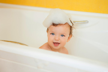 Smiling kid with foam and soap bubbles in bathroom.