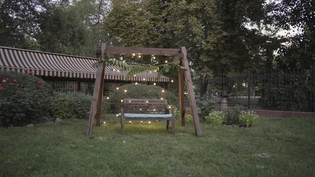 Wooden decorative bench under a wooden arch decorated with luminous bulbs on a green lawn