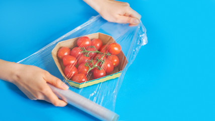 Woman using food film for food storage on a white table. Roll of transparent polyethylene food film...