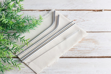 Four reusable metal cocktail straws (straws) on a light wooden background.