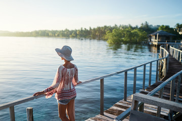 Vacation on tropical island.  Back view of young woman in hat enjoying sunset sea view from wooden bridge terrace, Siargao Philippines