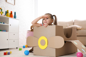 Cute little child playing with cardboard plane at home