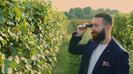 Man on vineyard with special instrument. Side view of elegant bearded man using refractometer...