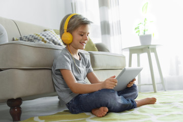 Cute little boy with headphones and tablet listening to audiobook at home