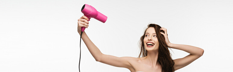 panoramic shot of cheerful girl drying hair with hair dryer isolated on white