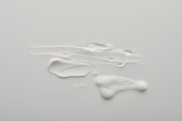 Top view of gel and cosmetic cream brushstrokes with soap foam on grey background