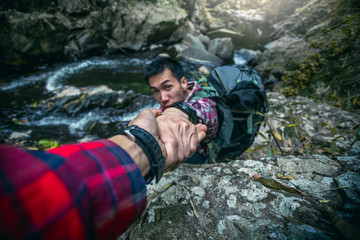 Man giving helping hand to friend to climb mountain on river