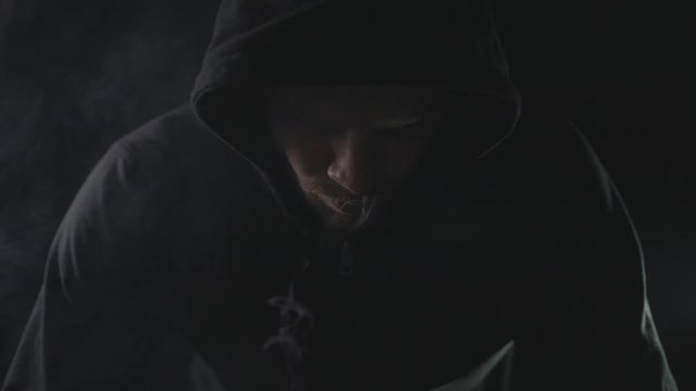 man in black hoodie smoking vape in dark room. blowing smoke