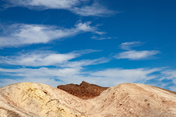 Sinuous breast shaped white rocks in the foreground and a peak of a brown mountain in the background in the desert of Death Valley national park