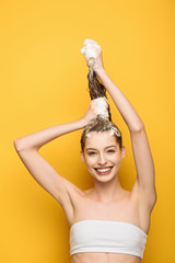 happy girl looking at camera while washing long hair on yellow background