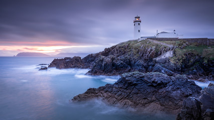 Fototapeta na wymiar Twilight yields to dawn, sunrise at Fanad Head Lighthouse with blurred water of Atlantic Ocean. Wild Atlantic Way, Donegal, Ireland