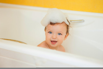 Smiling kid with foam and soap bubbles in bathroom.