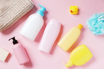 Beige towel, shampoo bottle, liquid soap, shower gel, hair balm and conditioner, blue sponge and rubber duck on a pink background. Flat lay toiletries essentials, baby care cosmetic products