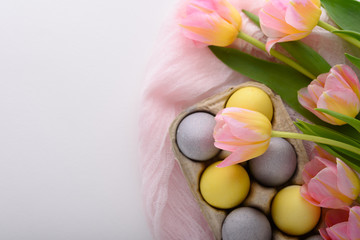 yellow and blue Easter eggs in cardboard box on pink fabric on white background