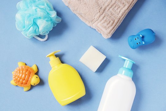 Flat lay photography baby care bath products. Sponge puff, yellow liquid soap package, shampoo bottle, towel, rubber toys on a blue background